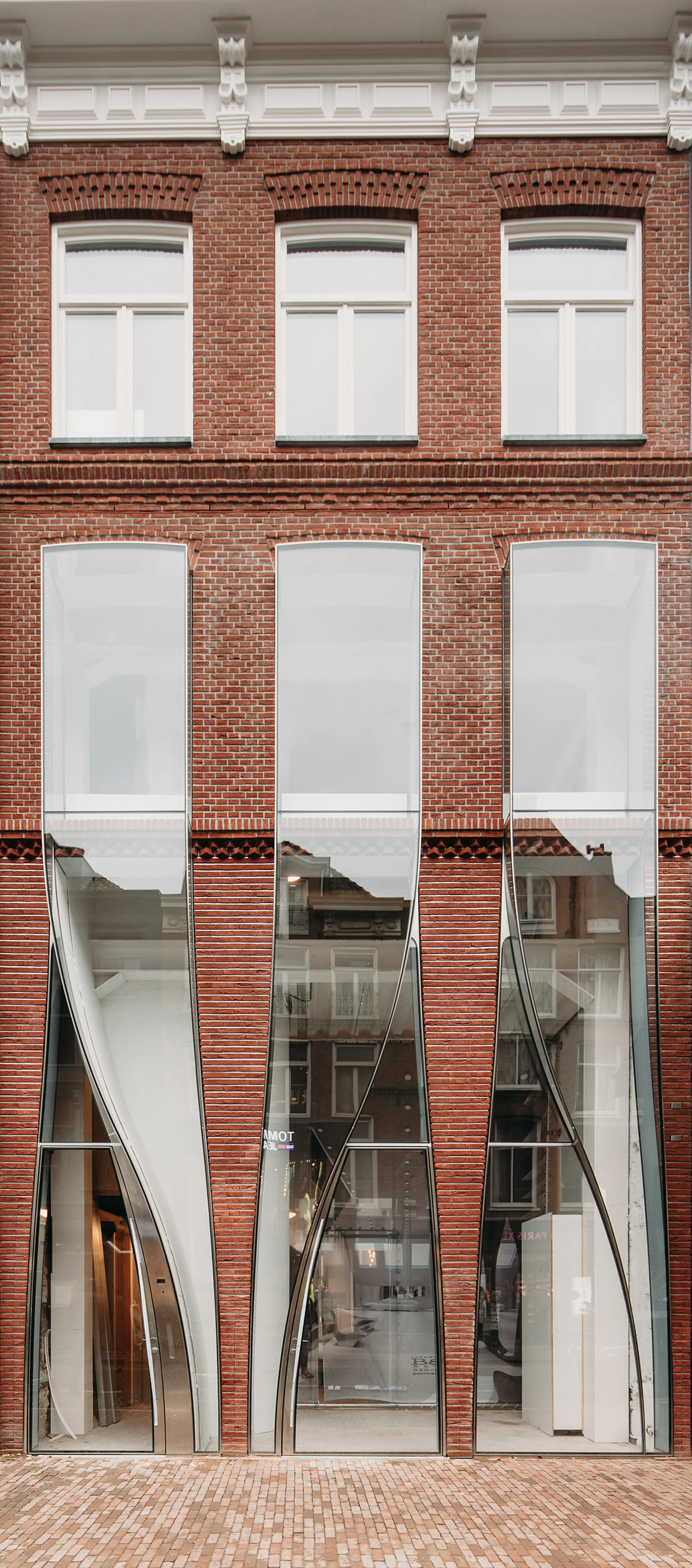 The façade: brick above, glass falling like cloth below